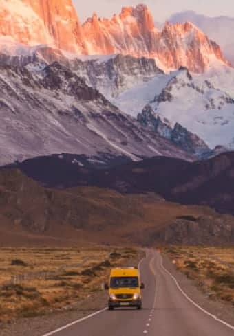 Gelber Camper auf einer offenen Straße vor dem schneebedeckten Fitz-Roy-Massiv in Patagonien